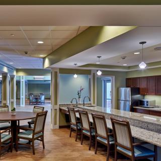 A modern kitchen and dining area featuring a long counter with bar stools, a circular dining table with chairs, and contemporary lighting fixtures.
