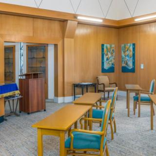 A meeting room featuring wood paneling, tables and chairs with blue upholstery, and artwork on the walls.