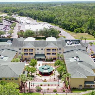 Aerial view of a large building complex surrounded by lush greenery and a parking lot.