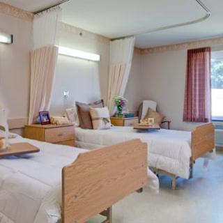 A well-lit patient room in a hospital featuring two beds, curtains, and a cozy atmosphere.