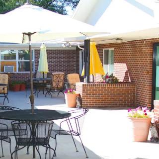 A sunny patio area with tables, chairs, and umbrellas outside a brick building.