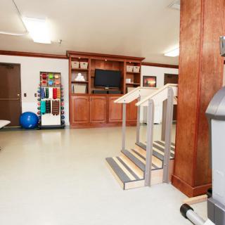 A spacious indoor gym area equipped with exercise equipment, stairs for rehabilitation, and a television.