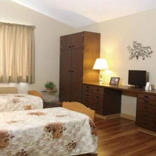 A cozy bedroom featuring twin beds, a desk with a lamp, and a wardrobe.