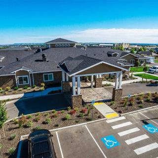 Aerial view of a building with a landscaped entrance and adjacent parking lot on a sunny day.