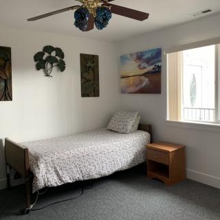 A minimalist bedroom with a single bed, nightstand, window, and wall art.