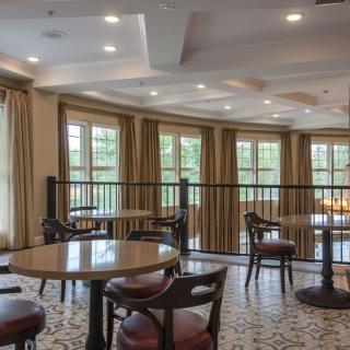 A cozy dining area with tables and chairs, illuminated by natural light from large windows.