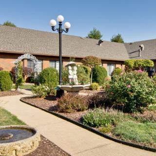 A beautifully landscaped garden featuring a stone pathway, fountains, and manicured bushes.