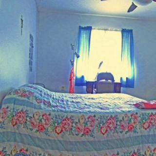 A bright bedroom featuring a floral quilt on the bed and blue curtains framing the window.