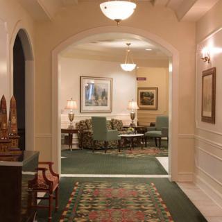 A warmly lit hallway leads into a traditionally decorated sitting area with green carpet and classic furniture.