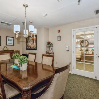 A cozy dining room with elegant furniture and decor, featuring a wooden table, upholstered chairs, a chandelier, and decorative plants.