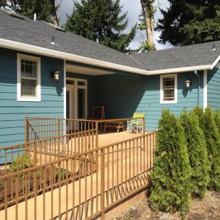 A charming blue house with a wooden deck and ramp, surrounded by lush greenery.