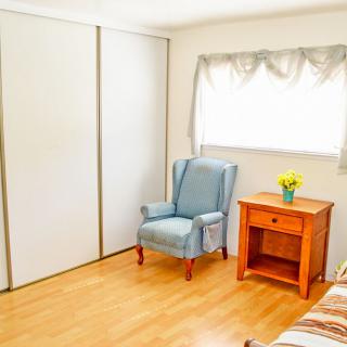A minimalist bedroom with a blue armchair and wooden nightstand beside a window.