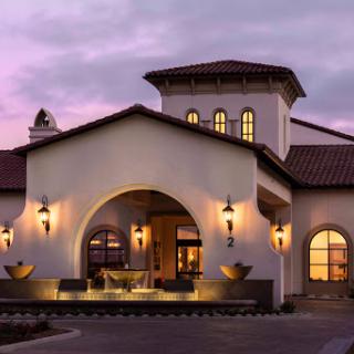 A stunning Mediterranean-style building illuminated during twilight, featuring elegant fountains and a warm ambiance.