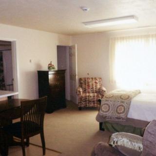 A cozy bedroom featuring a bed, chair, and dresser with ample natural light.