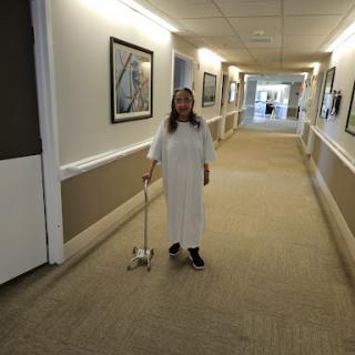 A patient walking down the hospital corridor with a cane.