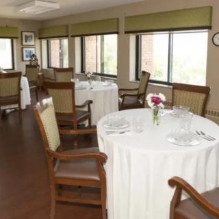 A well-lit dining room with round tables and chairs, set for a meal.