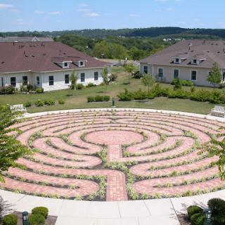 A peaceful labyrinth garden surrounded by greenery and buildings.