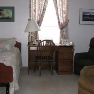 A cozy bedroom featuring a wooden desk with a lamp, positioned in front of a window with floral curtains.