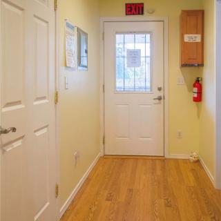 A hallway with wooden floors leading to a door with an exit sign above it and a fire extinguisher to the side.