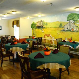 A cozy dining room with tables and chairs, featuring a colorful farm-themed mural on the wall.