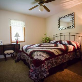A cozy bedroom with a bed featuring a decorative patterned blanket, a mirror above the headboard, and a small desk by the window.