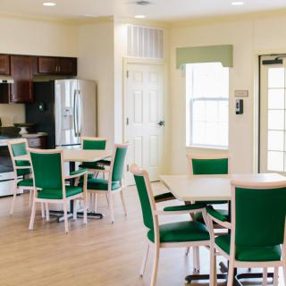 A modern dining area with green chairs and tables, adjacent to a kitchen with stainless steel appliances.