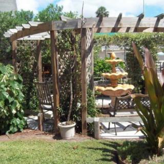 A lush garden with a wooden pergola and a decorative fountain surrounded by greenery.