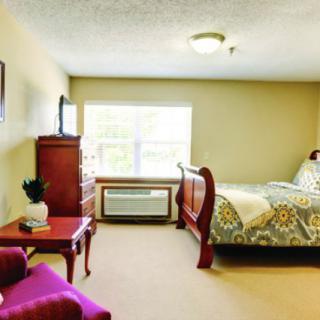 A cozy bedroom with a large bed, dresser, armchair, and a window providing natural light.