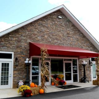 A storefront with a brick exterior and red awning decorated with fall-themed items, including pumpkins and gourds.