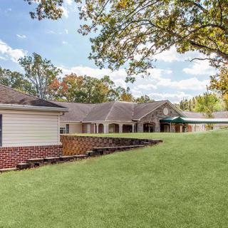A peaceful residential building surrounded by a well-maintained lawn and trees under a partly cloudy sky.