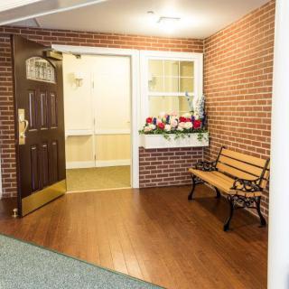 An interior space with a wooden door, adjacent brick wall, window with flower box, and a decorative bench.