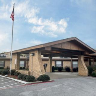 A single-story building with a covered entrance and an American flag in the parking lot.