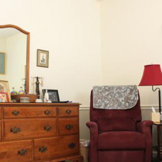 A cozy corner with a wooden dresser, red armchair, and lamp.