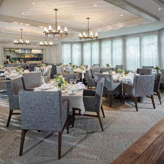 An elegantly set dining room with neatly arranged tables and comfortable chairs, featuring stylish chandeliers and decor.
