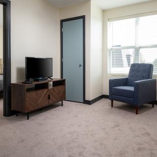 A cozy living room with a television, armchair, and large window.