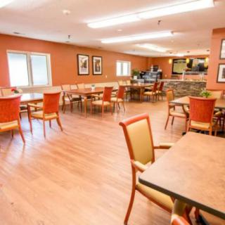 A spacious and well-lit dining area with multiple tables and chairs arranged neatly on a wooden floor.