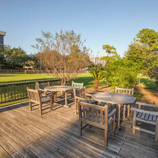 A sunny outdoor deck with wooden tables and chairs overlooking a lush garden.