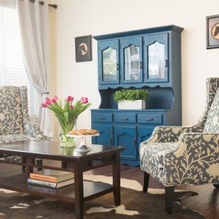 A cozy living room with patterned armchairs, a wooden coffee table, and a striking blue cabinet, complemented by floral decorations.