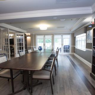 A modern conference room with a long table and several chairs, well-lit by natural light from large windows.