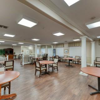 A spacious dining area with multiple tables and chairs, featuring wooden flooring and ceiling lights.