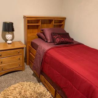 Cozy bedroom with a single bed, red bedding, and wooden furniture.