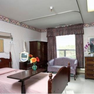 A hospital room with a patient bed, television, and furniture.