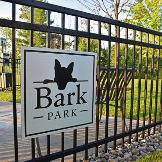 A sign on a fence reading 'Bark Park' with a silhouette of a dog's head, indicating a designated dog park area.