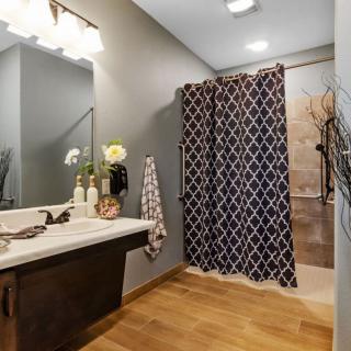 A modern bathroom with wooden flooring, featuring a stylish sink area and patterned shower curtain.