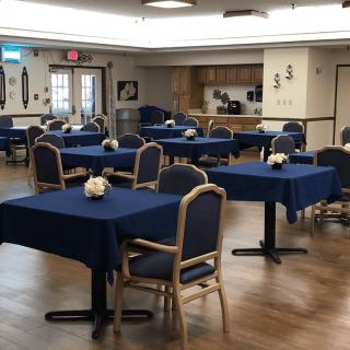 An empty dining room with tables covered in blue tablecloths and neatly arranged chairs.