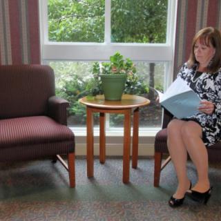 A woman in business attire reads a folder while sitting in a waiting room.