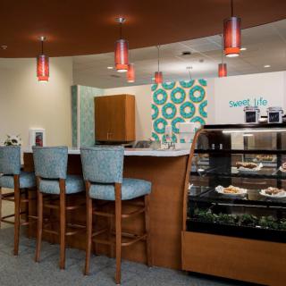 A cozy cafe interior with seating at a counter and a display case filled with treats.