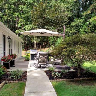 A peaceful backyard patio with outdoor furniture and a large umbrella, surrounded by lush greenery.