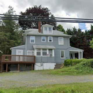A two-story residential house with a deck, surrounded by greenery under a cloudy sky.