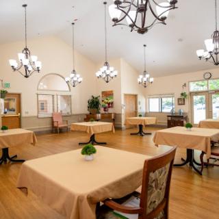 A spacious and elegantly designed dining area with tables set for guests, featuring chandeliers and a warm wooden floor.